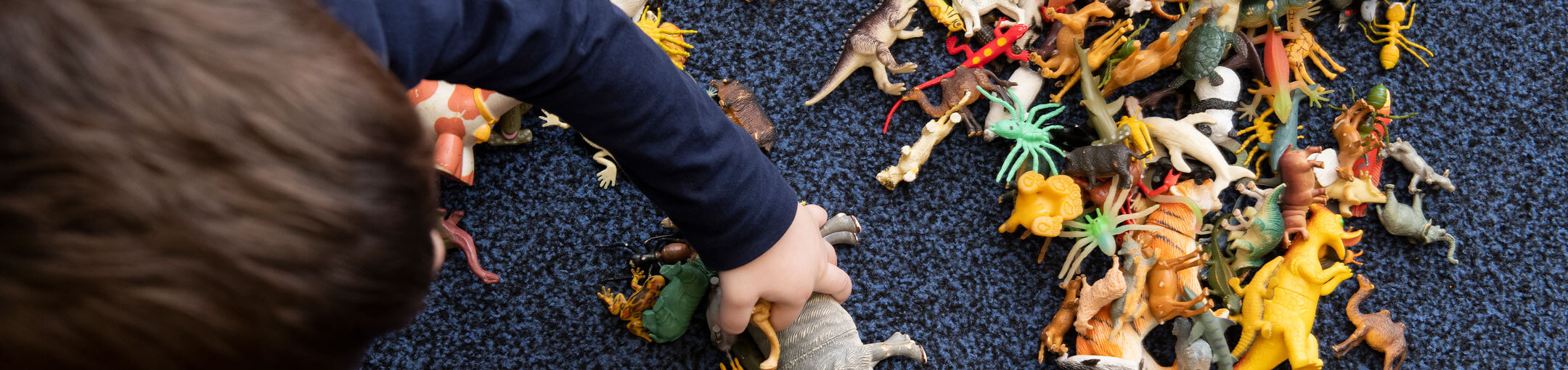 A toddler playing with a dinosaur toys on the floor.