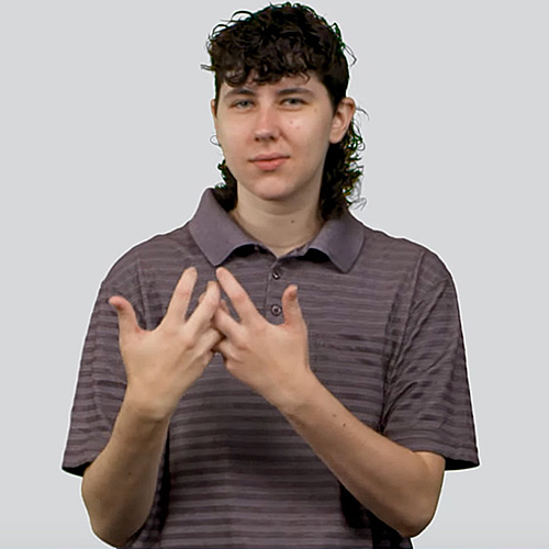 A person is shown with short, curly dark hair styled in a mullet. They are wearing a collared, short-sleeved, gray and purple striped shirt. The person is holding their hands together in front of their chest with fingers partially interlocked, they are signing 'roommate.' The background is plain and light gray.