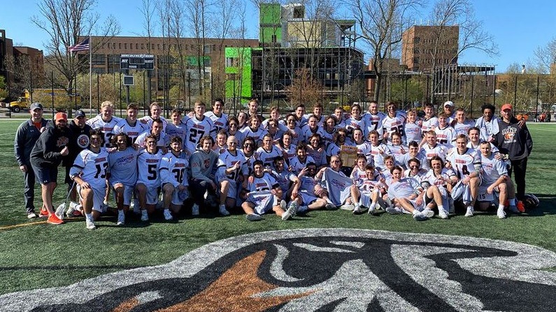 Group of lacrosse players and coaches posing for photo.
