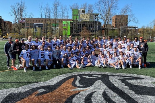 Group of lacrosse players and coaches posing for photo.