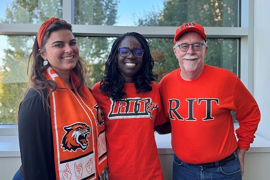 Three people wearing RIT gear smile for a photo.