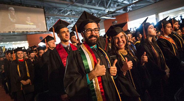 Graduates wearing their caps and gowns smiling at a graduation ceremony