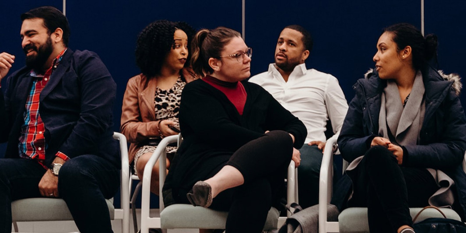 ﻿Group of diverse people sitting in two rows of chairs while conversing