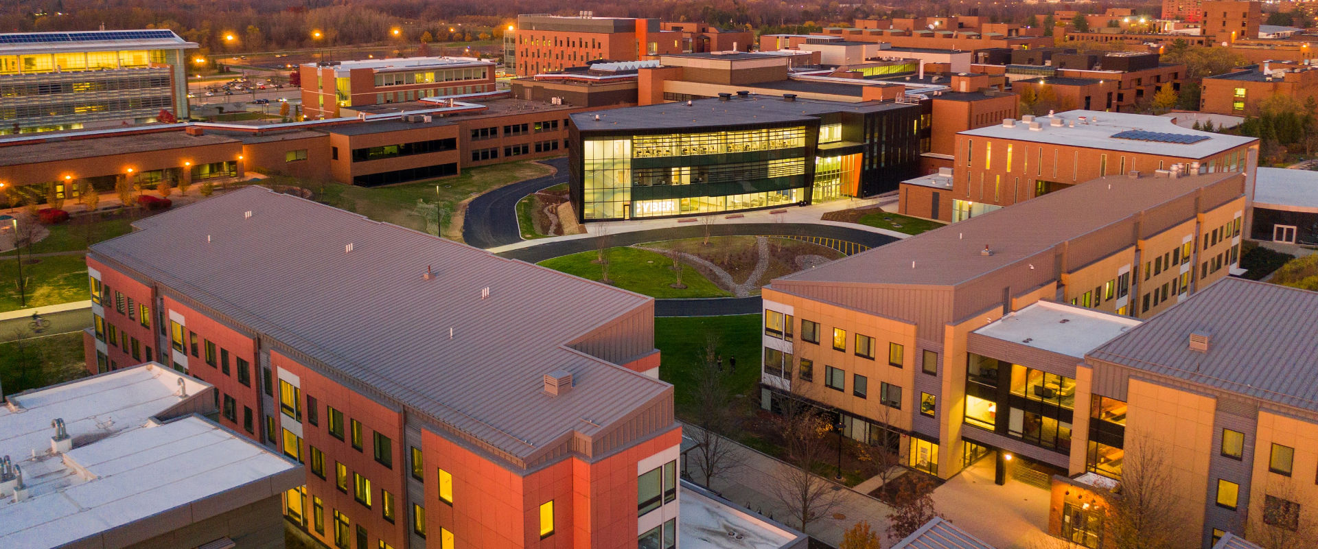 Aerial view of RIT campus during twilight, featuring illuminated buildings, a central green space.