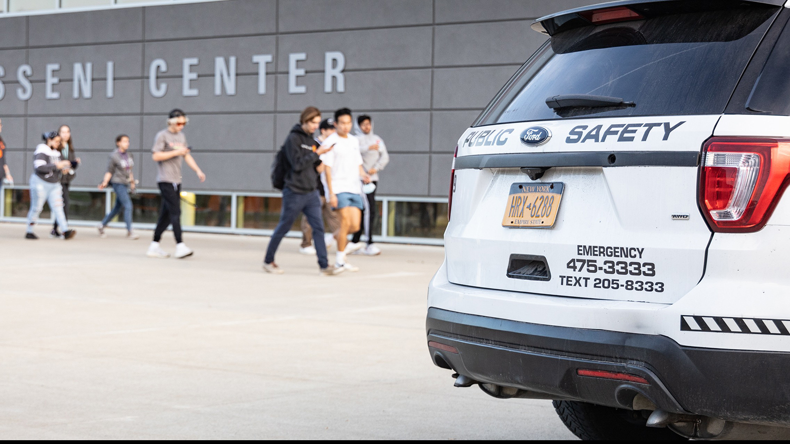 Students walking in front of the Gene Polisseni Center with a public safety vehicle in the foreground