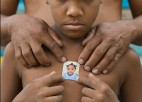 A shirtless boy holds up a small photo across his chest.