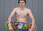 a teenager poses shirtless while holding a skateboard.