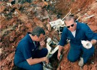 Two men look through debris from an airplane crash.