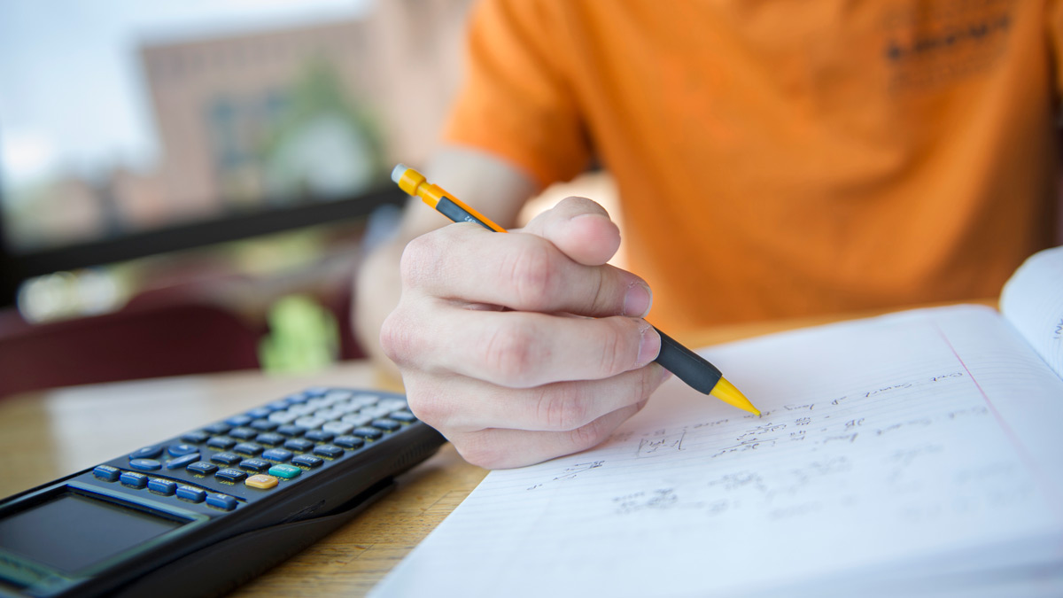 Close up of hand writing in a notebook with a mechanical pencil and a graphing calculator.