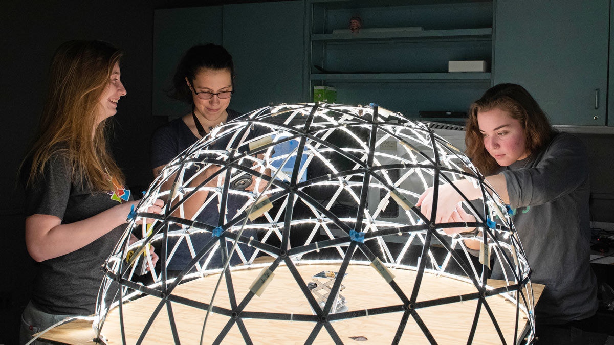 Three students taking images of an object in a lighting structure that removes shadows.