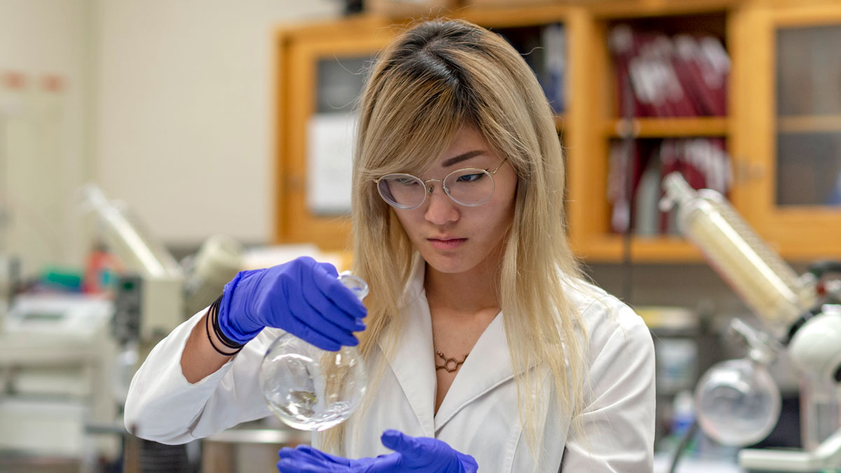 A purple-gloved students looks at the contents of a beaker.