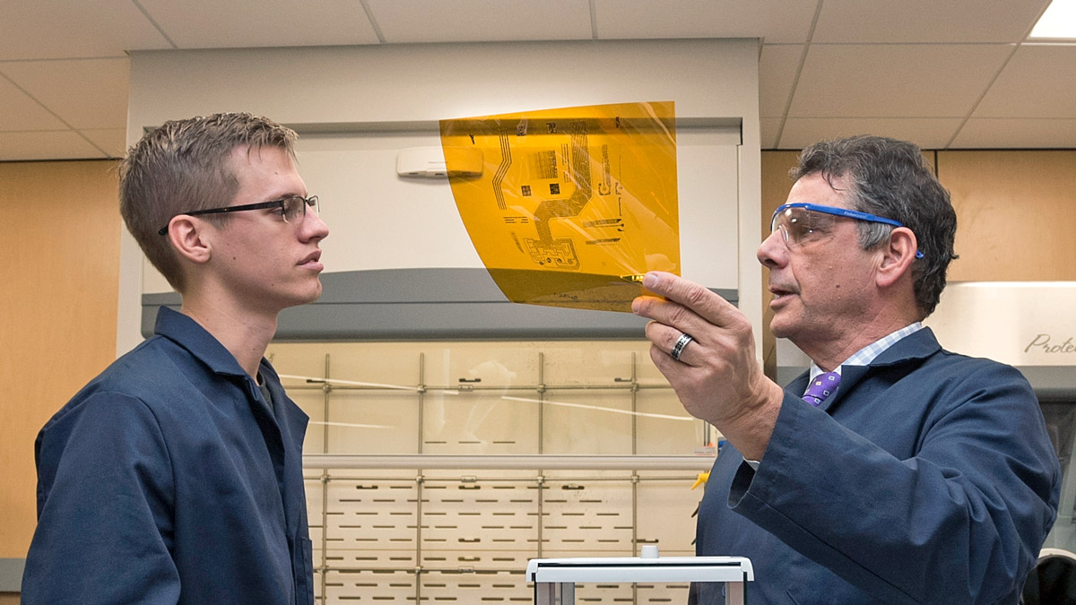 Student and professor talk over a schematic printed on amber-colored cellophane.