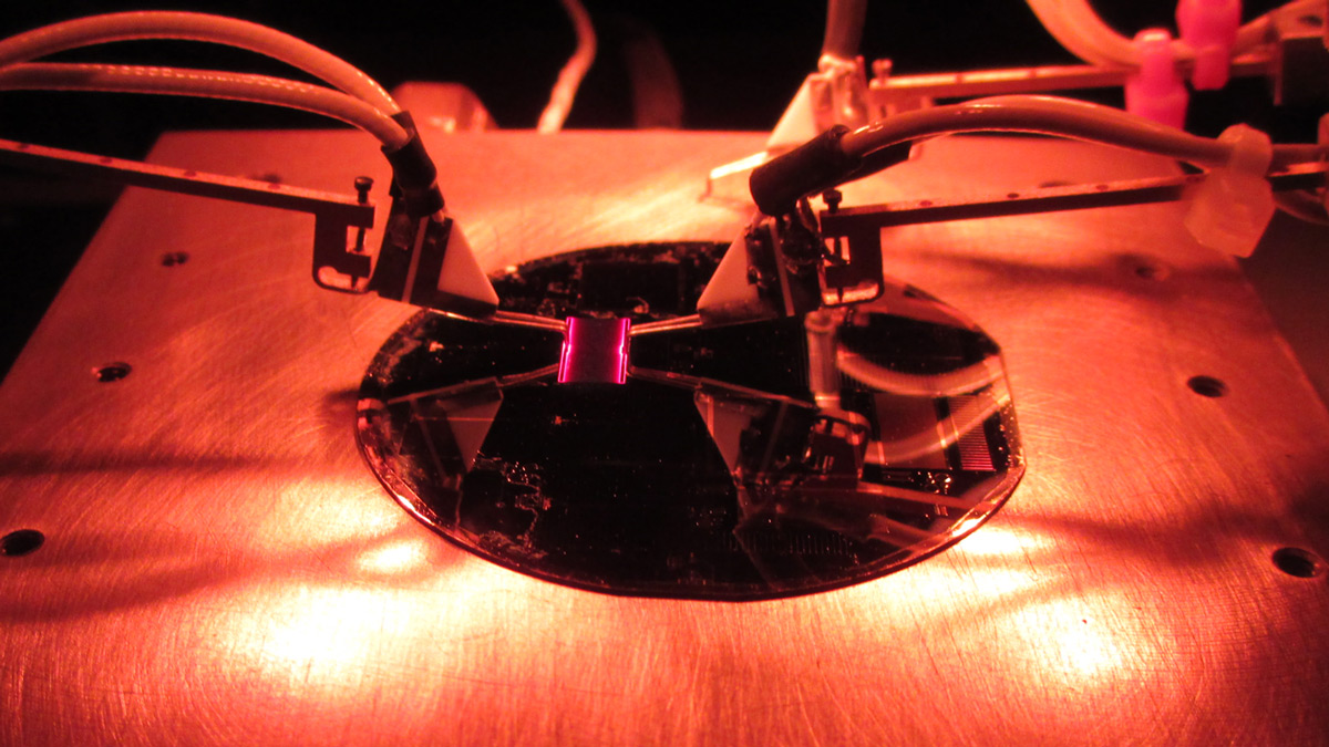 A close-up photo of clamps holding something purple and square over a reflective plate.