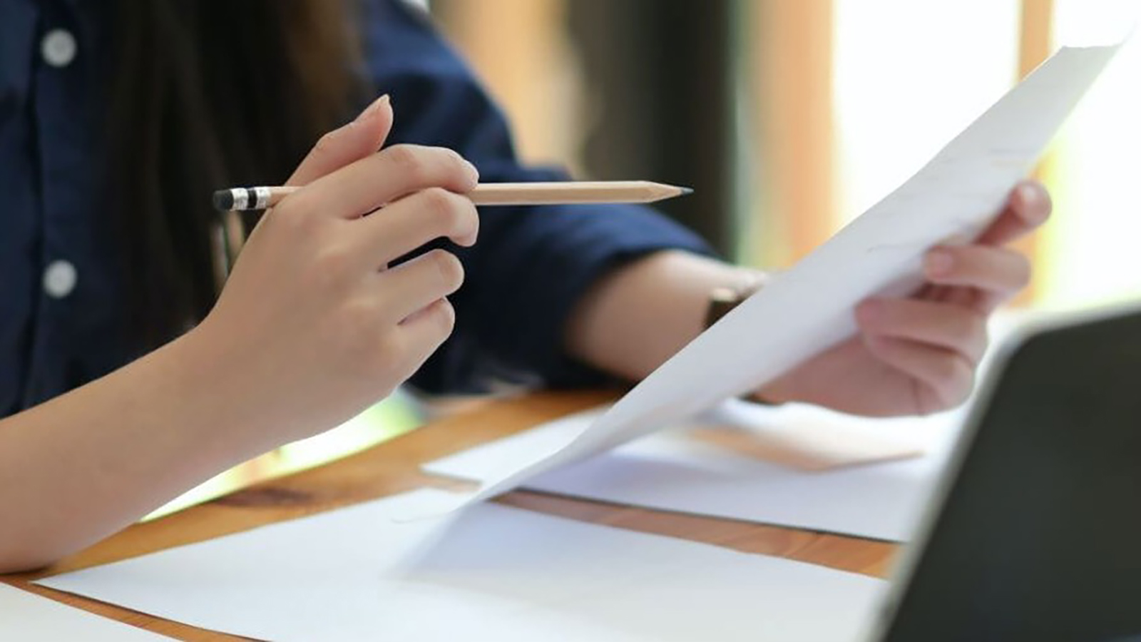 A closeup of a person sitting at a desk in front of papers and a laptop.