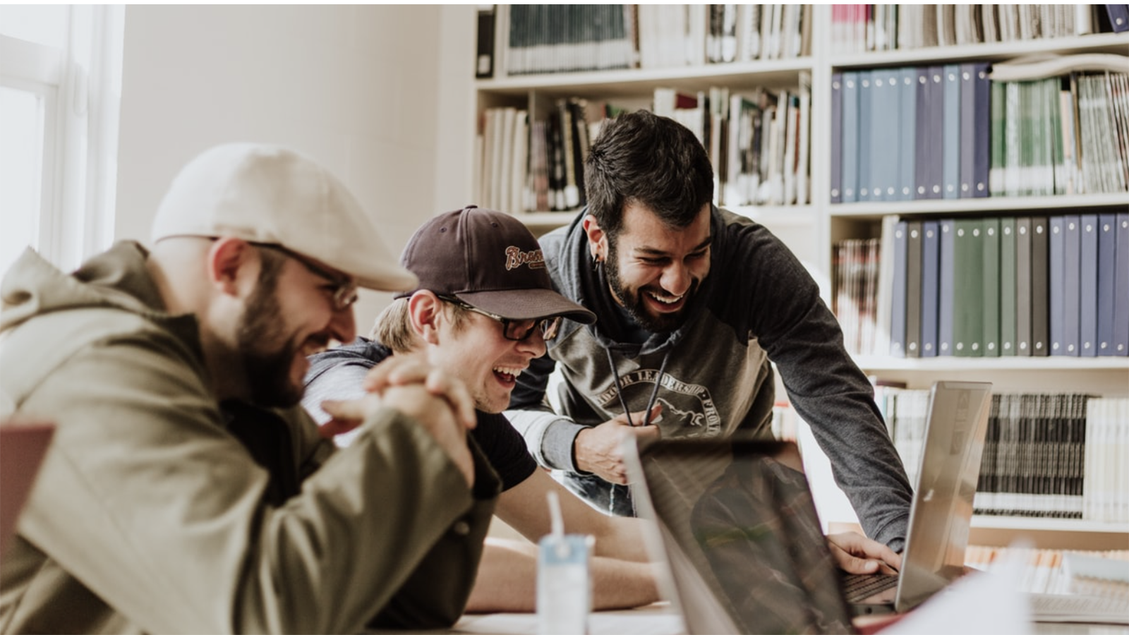 Three friends enthusiastically working on a laptop with a person to the right minding their own business.