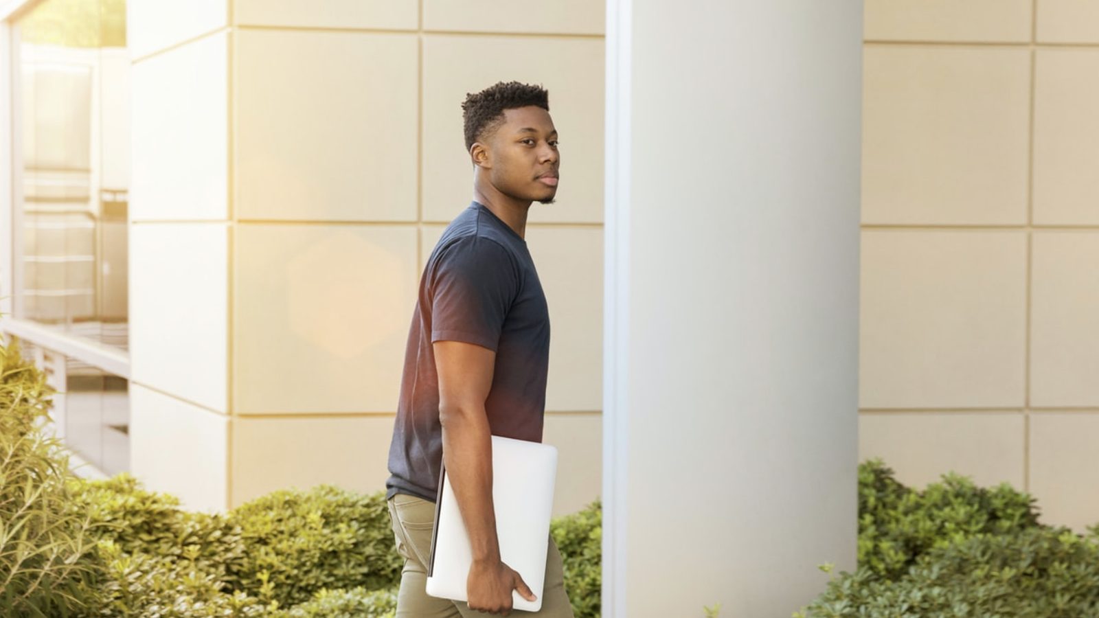 Undergraduate student walking with a laptop outdoors 