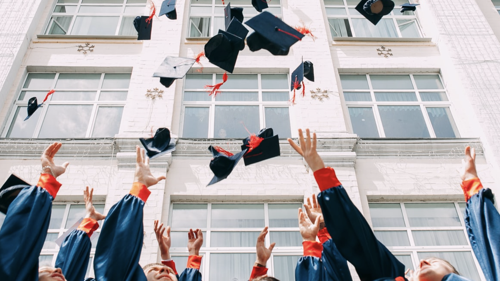 Graduation caps being tossed in the air by students in front of a building with large windows