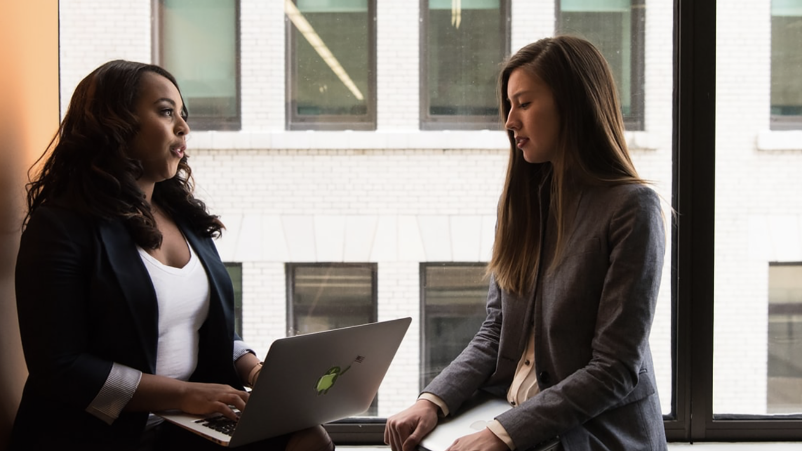 Two women sitting in front of a window discussing about finances