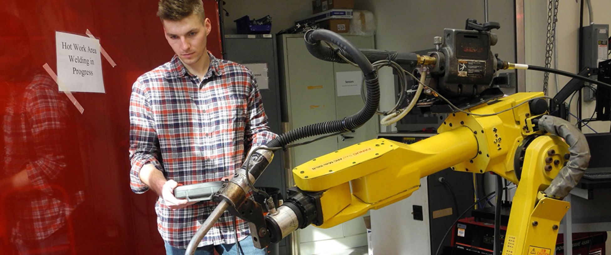 Student works with a radio-controlled, yellow, mechanical arm.