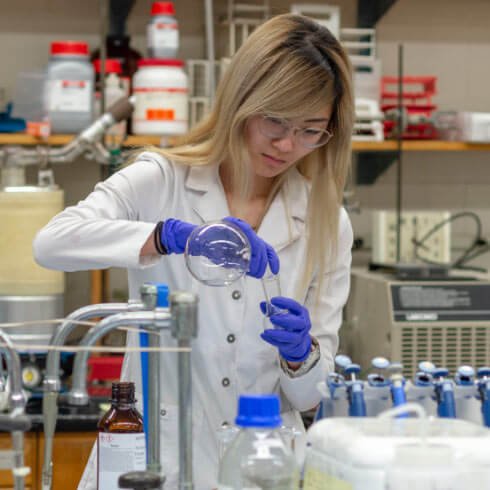 An RIT researcher pouring liquid from a beaker to a test tube.