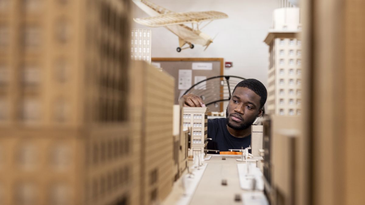 A student working carefully on a detailed architectural model of a cityscape.