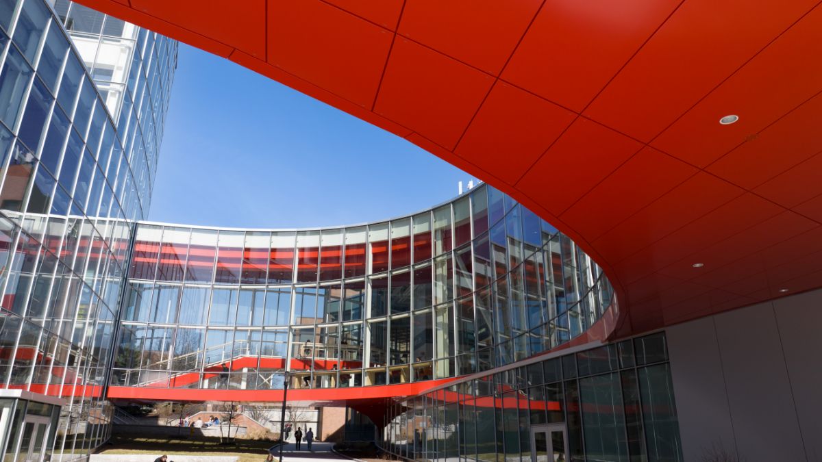 The architectural design of a building with red accents and curved lines under a bright blue sky.