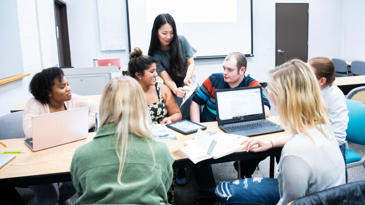 A group of students engaged in a collaborative classroom activity, working together with laptops and notebooks.