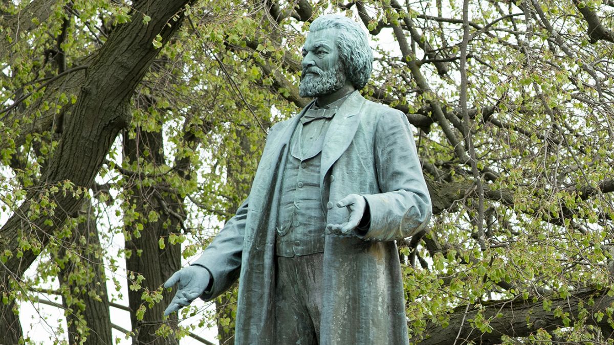 A bronze statue of Frederick Douglass surrounded by trees with spring foliage.