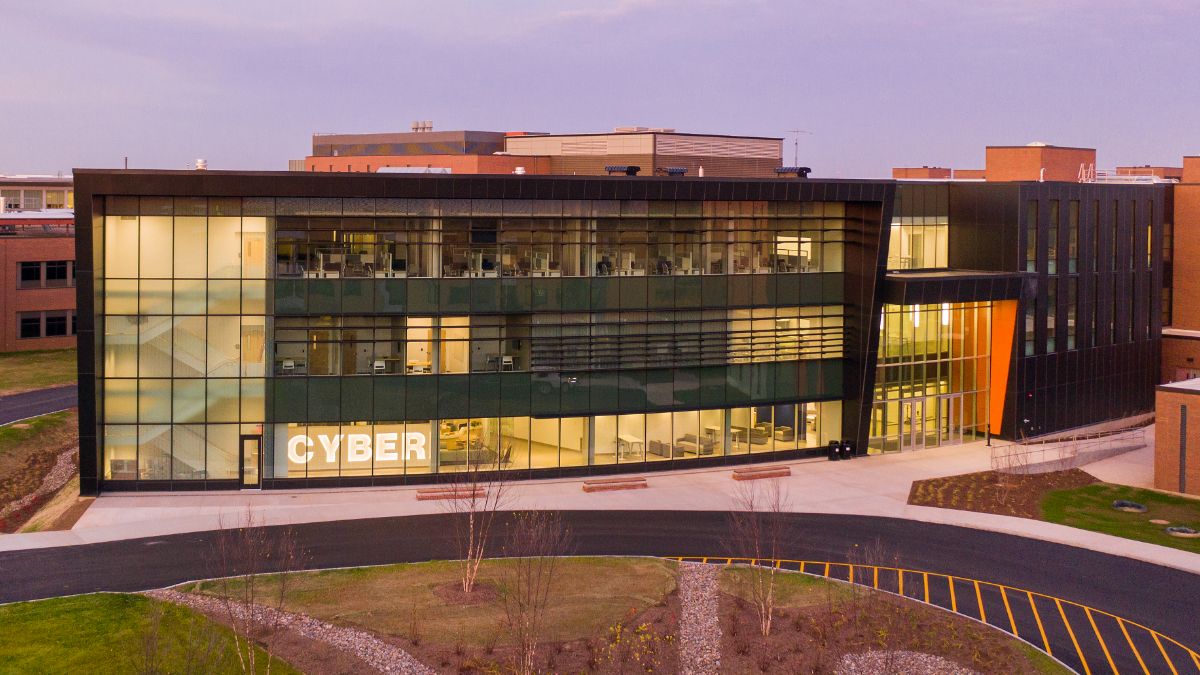 Exterior view of the R I T Cybersecurity building, featuring glass walls illuminated at dusk.