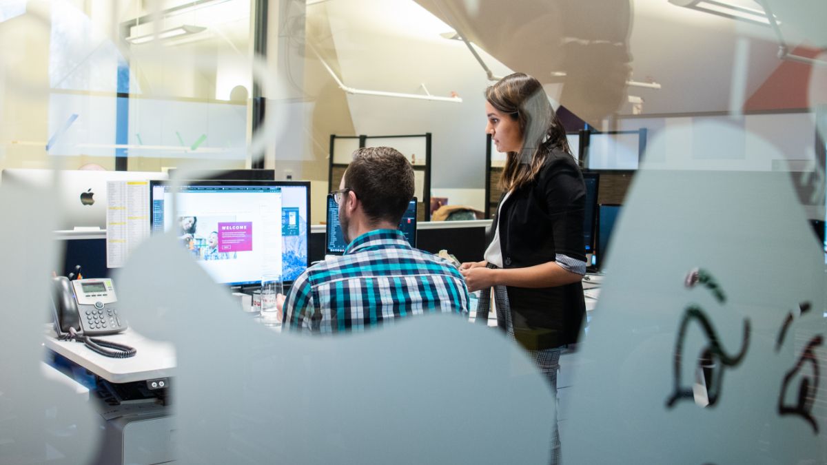 Two students working together in an office space, with one offering guidance to the other.