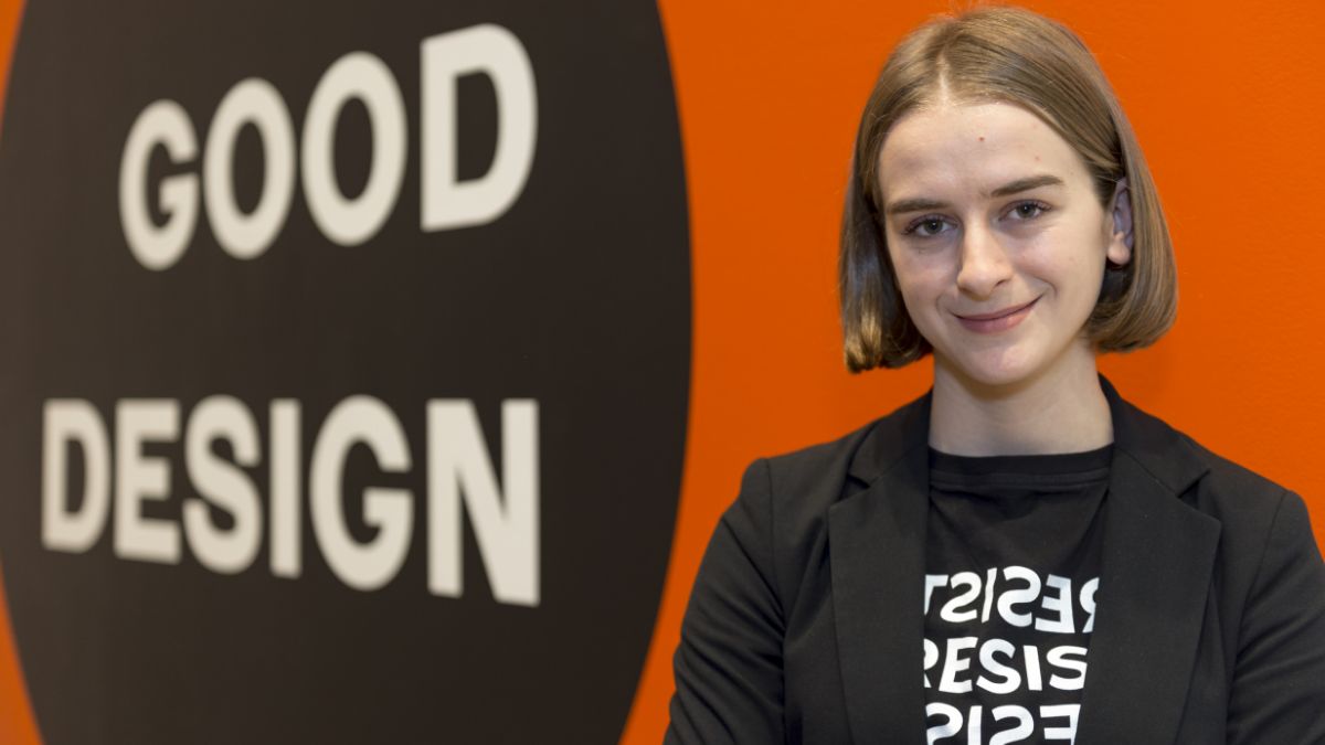 A portrait of a confident student standing in front of a large sign reading 'Good Design.'