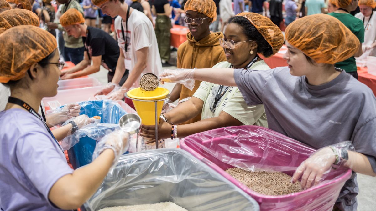 Students wearing hairnets working in an assembly line to package food for a donation.