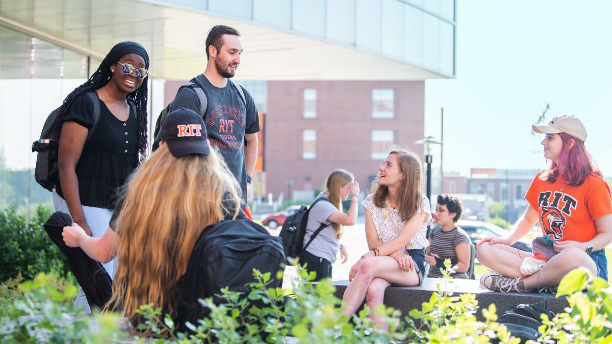 A group of R I T students socializing outdoors on campus, engaged in conversation.