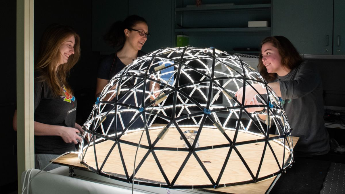 Students collaborating on a dome structure illuminated with L E D lights.