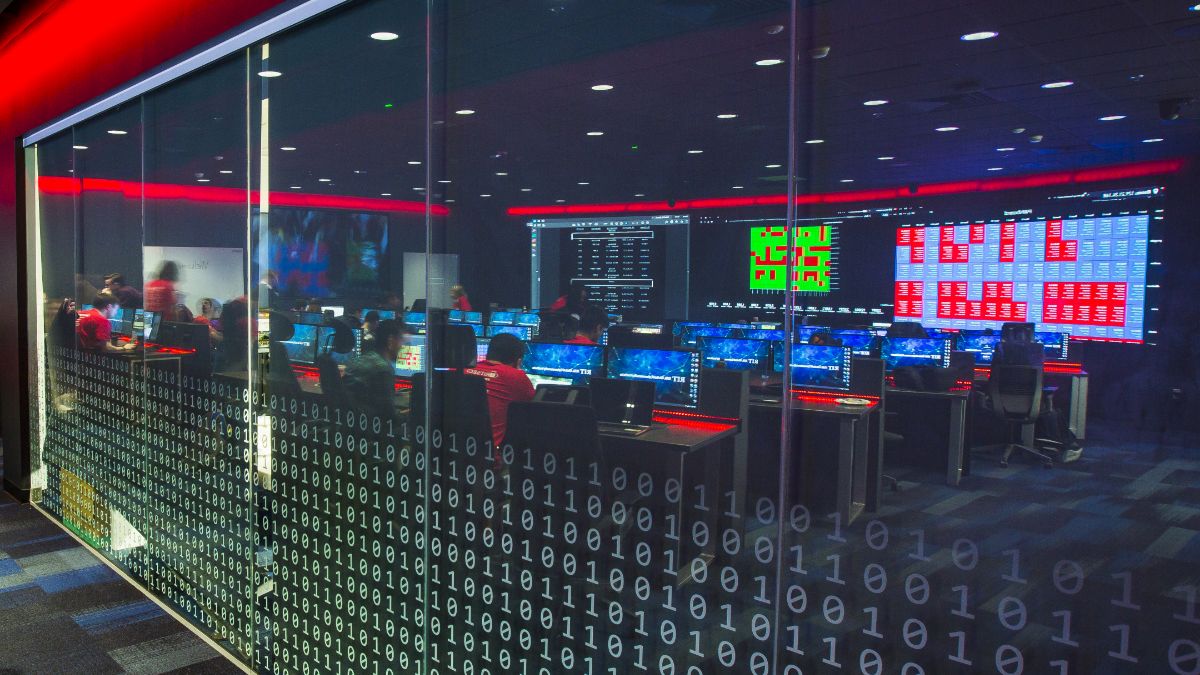 A cybersecurity control room filled with computer monitors and red accent lighting.