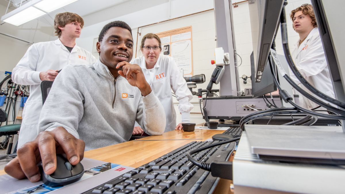 Professor and student watching another student work on a computer in a lab.