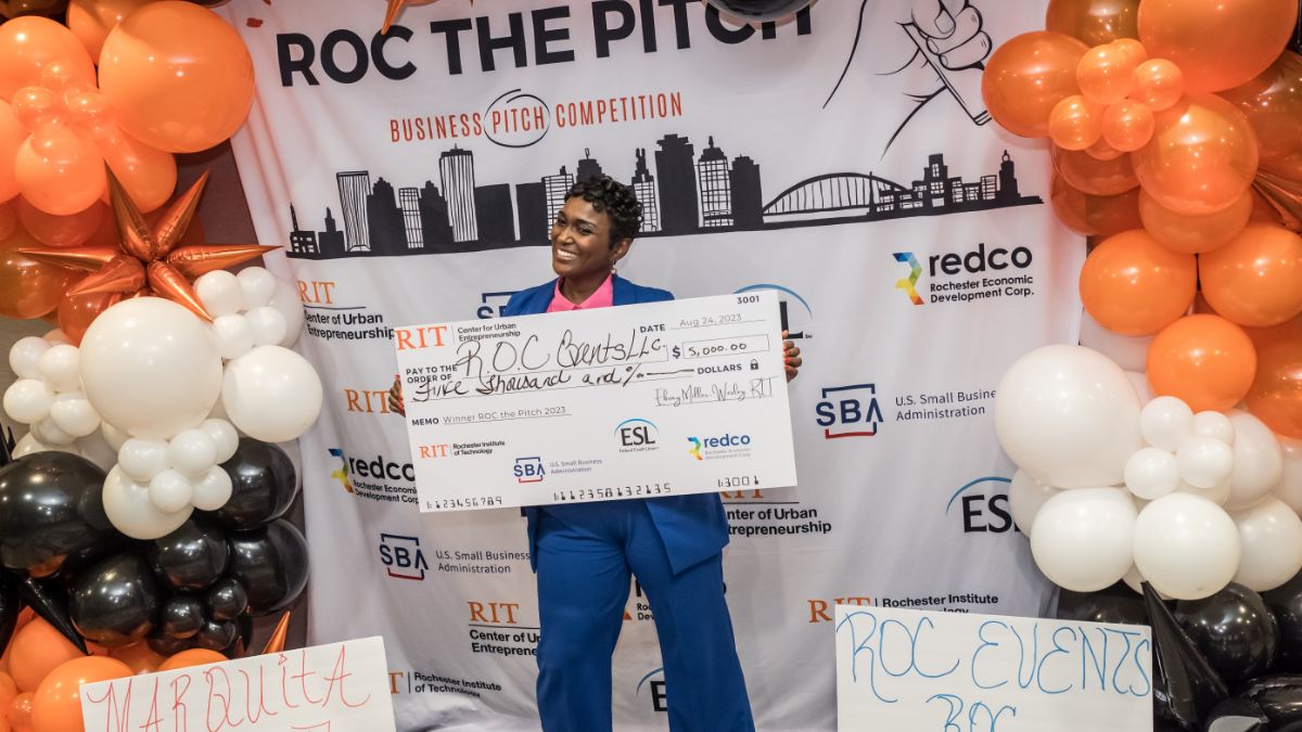 An entrepreneur proudly holding a giant check at a business pitch competition.