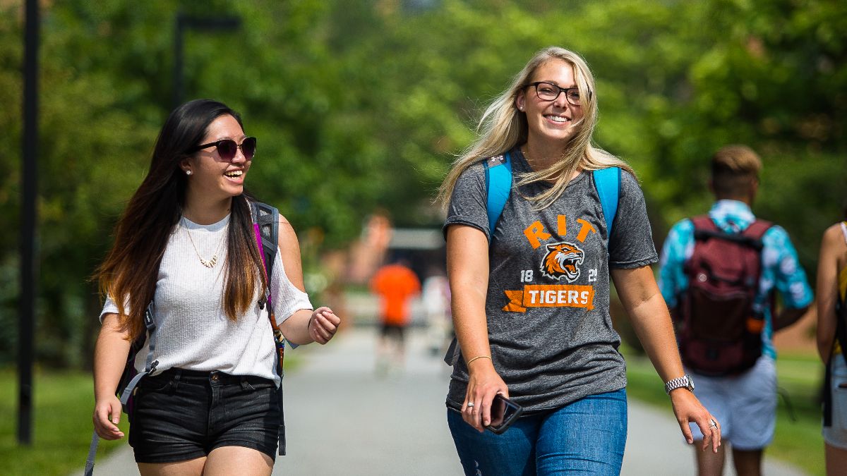 Two students walking across campus, smiling and enjoying the sunny day.