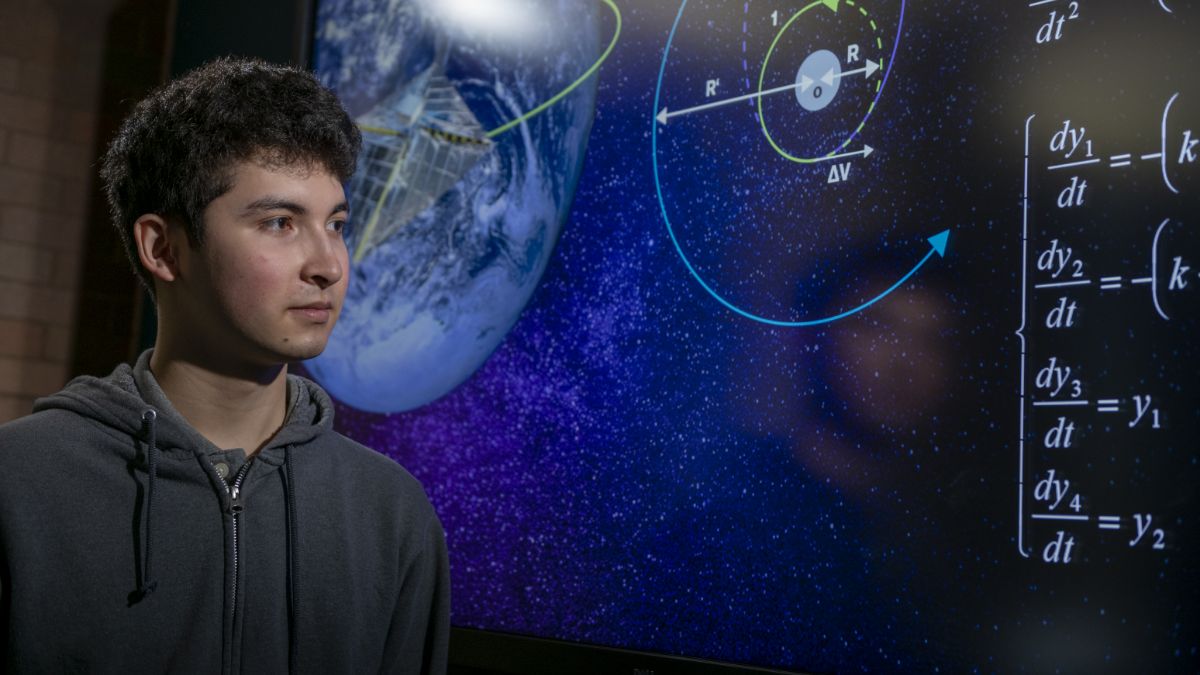 A student standing in front of a screen displaying astronomy-related equations and planetary diagrams.