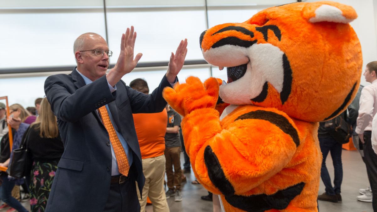 A person in a suit high-fiving R I T’s tiger mascot during a campus event.