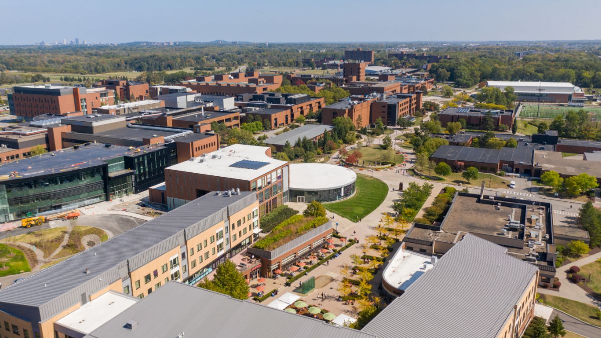 An aerial view of the R I T campus, showing brick buildings, green spaces, and walkways on a sunny day.