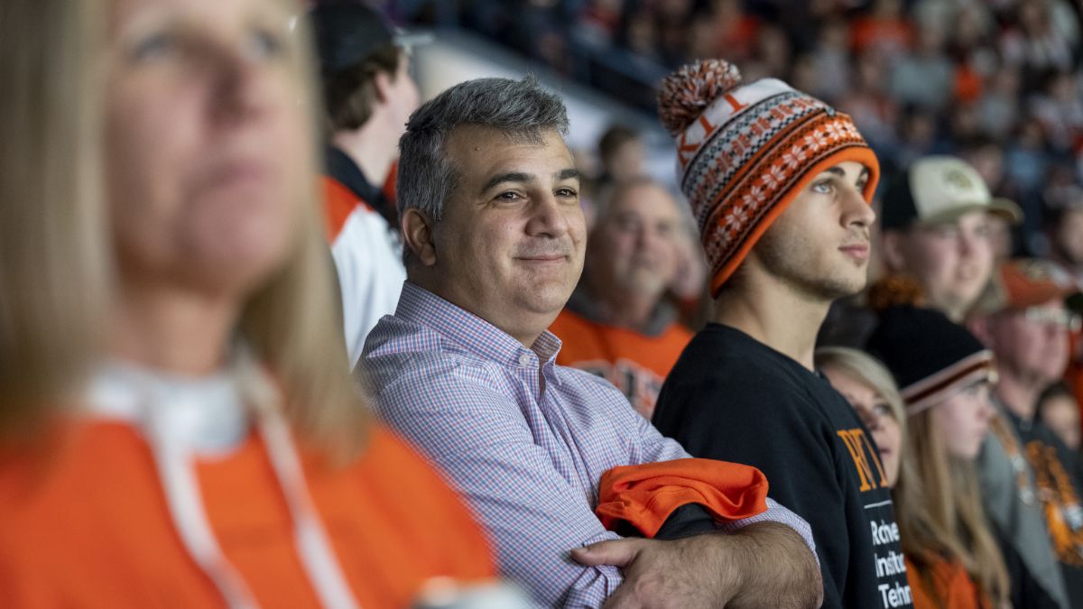 A group of spectators wearing R I T apparel, including one person in a winter hat, enjoying an event.