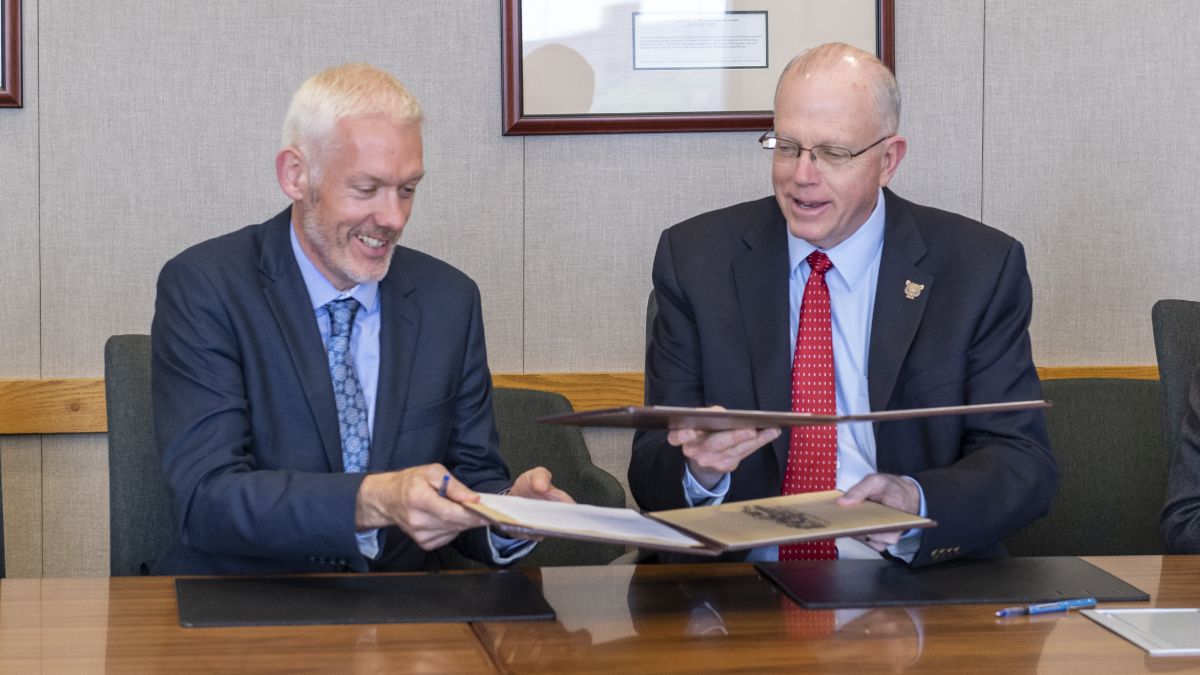 Two business professionals exchanging folders during a formal signing event.