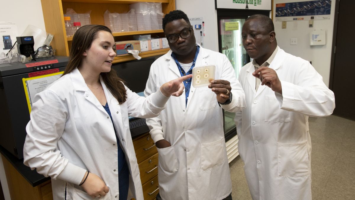 Researchers in a laboratory examining a sample while discussing their work.