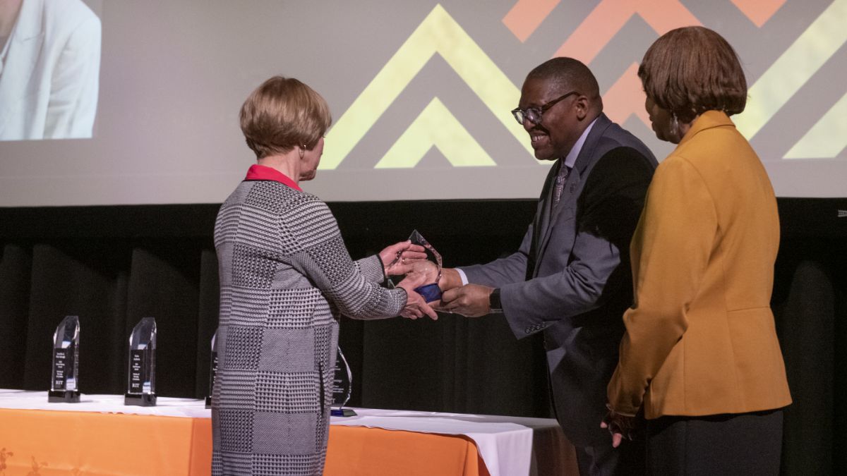 A formal award ceremony with a person receiving a trophy from a presenter on stage.