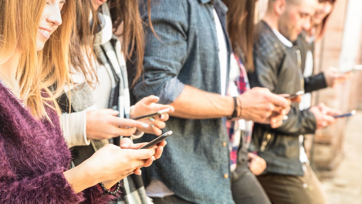 A group of young adults standing in a row, each focused on their smartphones.