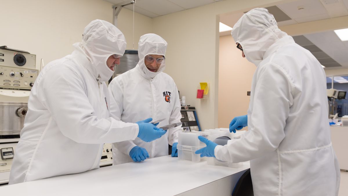 Scientists in protective suits working on materials in a cleanroom environment.