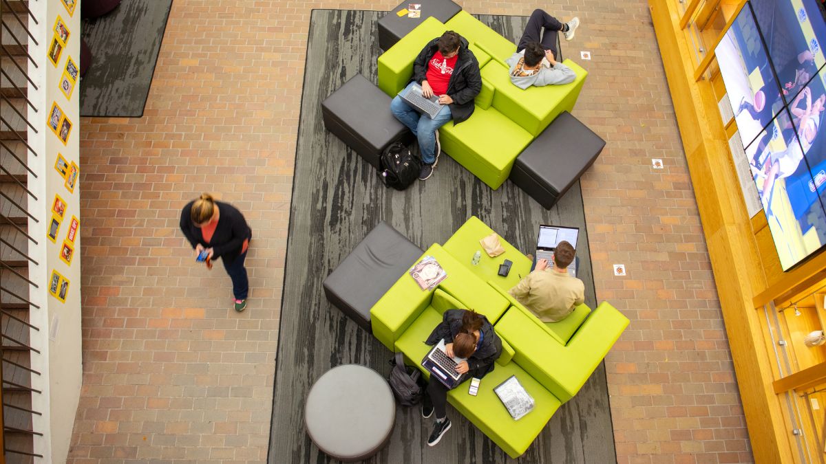 Overhead view of students studying and relaxing on modular green and black couches in a common area.