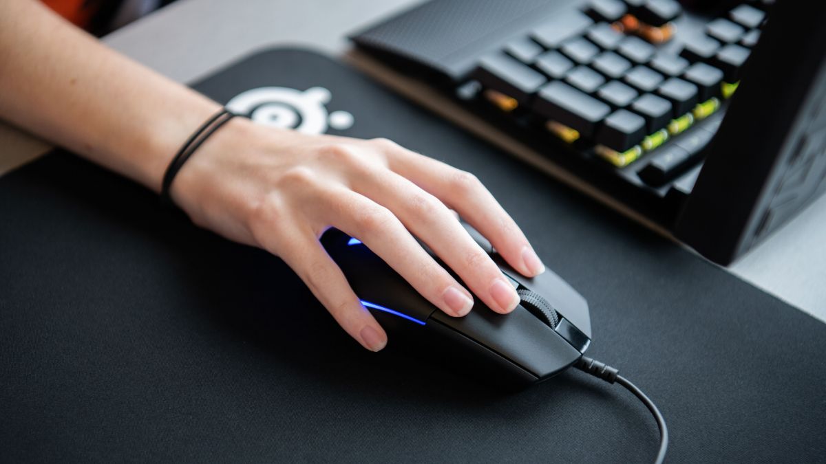 Close-up of a hand using a computer mouse on a black mousepad near a mechanical keyboard.