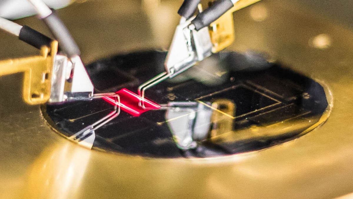 Close-up of research equipment with probes interacting with a small microchip on a metallic surface.